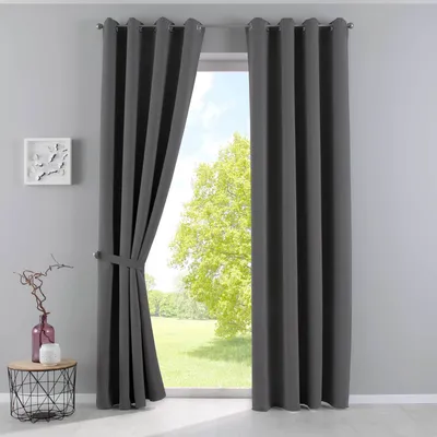A dark gray curtain is tied back with a fabric tie, revealing a bright green tree and blue sky outside a window.