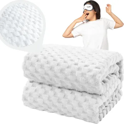 A woman wearing a sleep mask yawns, with a folded white blanket in the foreground and a close-up of the blanket's texture in the upper left corner.
