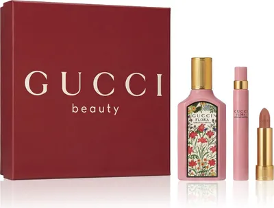 A Gucci beauty gift set containing a perfume bottle, a rollerball perfume, and a lipstick, presented next to a red Gucci beauty gift box.