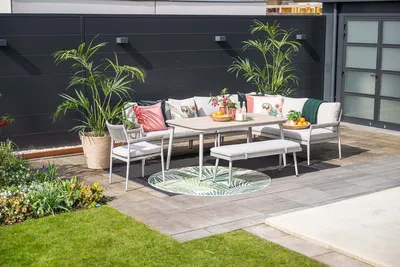 An outdoor dining set with a sofa, table, bench, and chairs on a patio next to a garden.