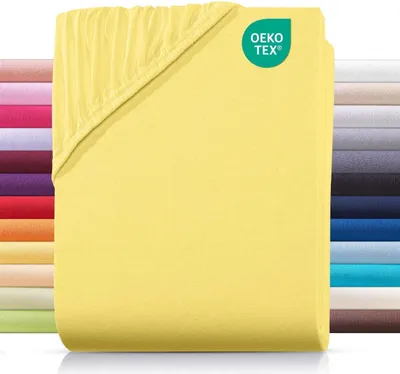 A folded yellow fitted sheet is shown with a stack of other colored sheets in the background.