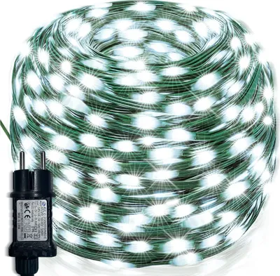 A coiled string of white LED lights on a green wire, with a black power adapter in the foreground.