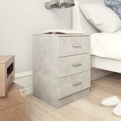 A gray bedside table with three drawers sits next to a bed. There are cardboard boxes on the floor to the left of the table. A book is on top of the table.