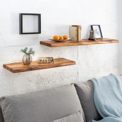 Two wooden shelves mounted on a white textured wall, decorated with various items, with a sofa in the foreground.