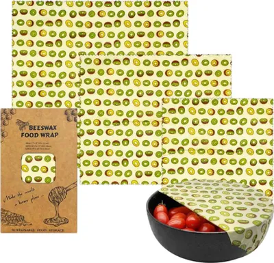 A set of beeswax food wraps with a kiwi pattern, along with packaging and a bowl of tomatoes covered by a wrap.