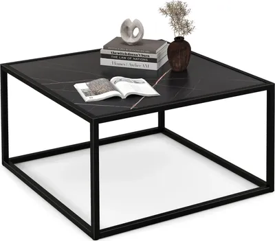 A black marble-look coffee table with a metal frame, decorated with books, a sculpture, and a vase with dried flowers.
