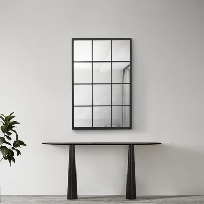 A modern console table with a large, multi-paneled mirror above it, set against a plain wall with a plant to the left.