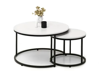 A pair of nesting round coffee tables with white tops and black metal frames, decorated with a small vase containing dried flowers and a black candle holder.