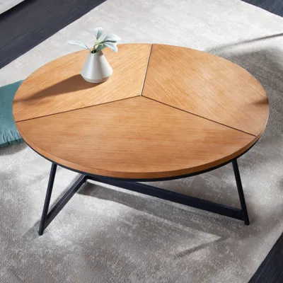 A round coffee table with a wooden top and black metal legs, placed on a rug.
