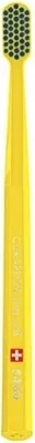 A yellow toothbrush with a patterned head and a small red and pink cross symbol on the body.