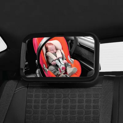 A baby is seen in a car seat through a car mirror.