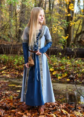 A young girl in a medieval-style dress stands in a forest during autumn.
