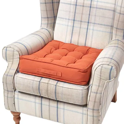 A tufted orange seat cushion is placed on a plaid armchair.
