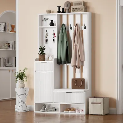 A white entryway organizer with hooks, shelves, and a bench is shown in a room with a light beige wall.