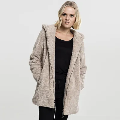 A woman wearing a sand-colored sherpa jacket and black top, standing against a white background.
