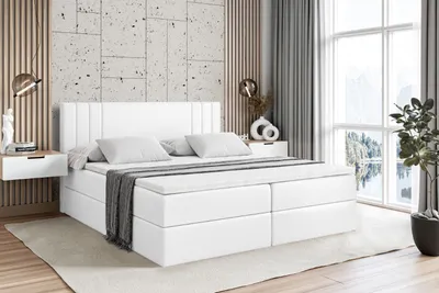 A white boxspring bed with a mattress and topper is shown in a bedroom setting.