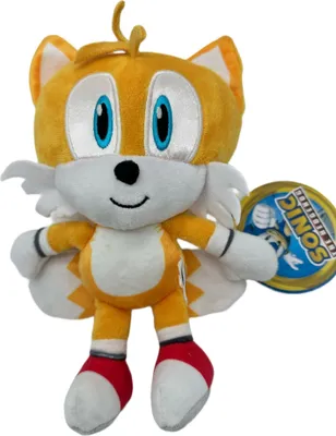 A plush toy of the character Tails from Sonic the Hedgehog is shown against a white background. A circular tag is attached to the toy's right arm.
