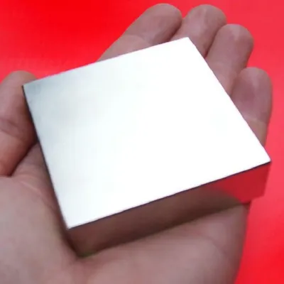 A hand holding a metallic cube against a red background.
