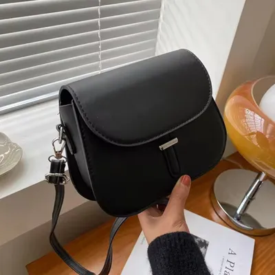 A black leather handbag is displayed on a wooden surface with blinds in the background.