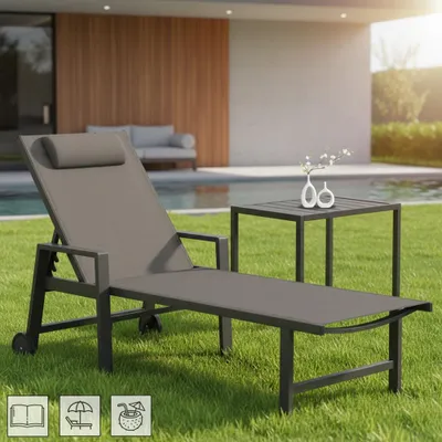A sun lounger and side table are set up on a lawn next to a swimming pool.