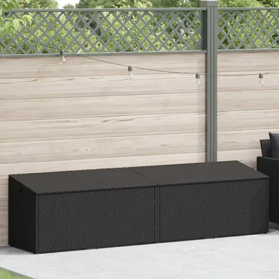 A black poly rattan storage box is placed on a patio in front of a wooden fence.
