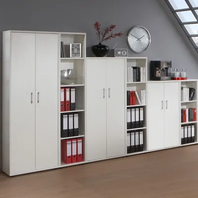 A white modular shelving unit with doors and open shelves, filled with binders and decorative items, in an office setting.