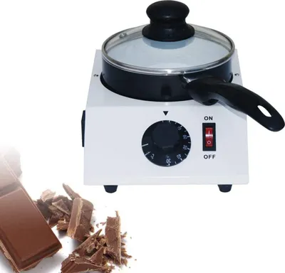 A chocolate melting pot with a lid, a dial, and an on/off switch, next to a bar of chocolate and some chocolate shavings.