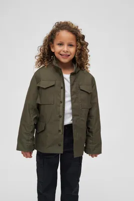 A young girl wearing a green jacket and black pants stands against a white background.