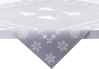 A close-up view of a grey tablecloth with a white snowflake and Christmas tree pattern, draped over the corner of a white table.