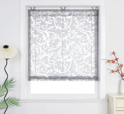 A window with a decorative Roman shade, a floor lamp, and a vase with branches on a nightstand.