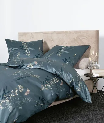 A bed with bedding and pillows, with a bedside table and lamp.