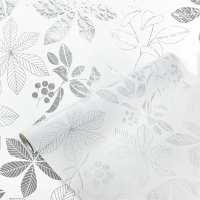 A roll of window film with a leaf pattern is shown, partially unrolled against a background of the same pattern.