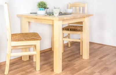 A wooden dining table with two chairs in a room with wooden flooring and white walls.