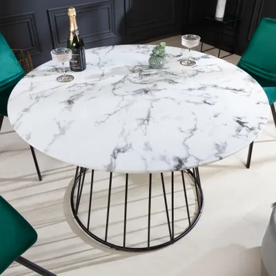 A round dining table with a marble-effect top and a black metal base, set in a dining room with green chairs.