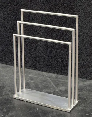 A silver towel rack with three bars stands on a dark floor in front of a black textured background.