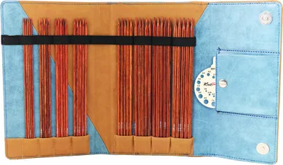 An open knitting needle case with various wooden knitting needles organized inside. A small circular gauge is visible in a pocket on the right side.