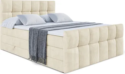 A beige upholstered boxspring bed with a mattress and pillows, shown from a diagonal angle.