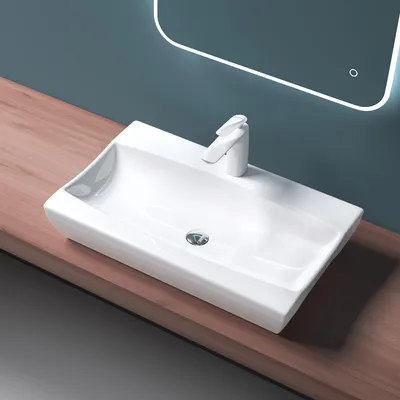 A white ceramic sink with a modern faucet sits on a wooden countertop, with a lit mirror in the background.