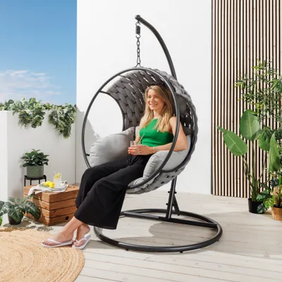A woman is relaxing in a hanging egg chair on a balcony.