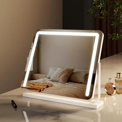A vanity mirror with integrated LED lighting is placed on a reflective surface, with a bedroom scene reflected in the mirror. Two perfume bottles are visible on the right side.