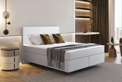 A modern bedroom with a white boxspring bed, a bedside table, and decorative lighting.