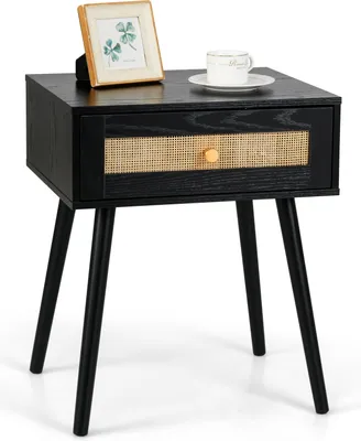 A black nightstand with a cane drawer front and a gold knob, shown with a framed picture and a cup of coffee on top.