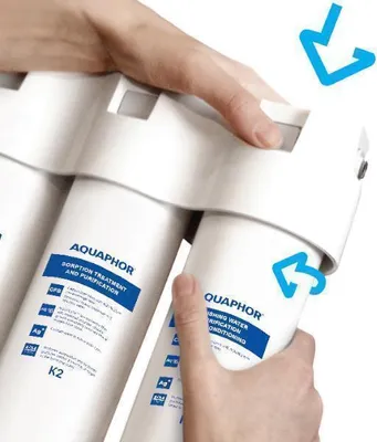 Hands are shown replacing a water filter cartridge in a water filtration system.