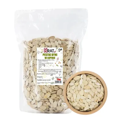 A bag of pumpkin seeds in their shells next to a wooden bowl filled with the same seeds.