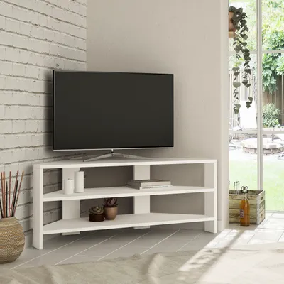 A white corner TV stand with a TV on it, placed in a room with a brick wall and a window.
