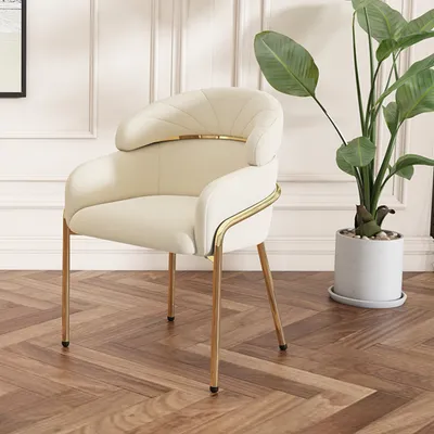 A beige armchair with gold legs sits on a wooden floor next to a potted plant.