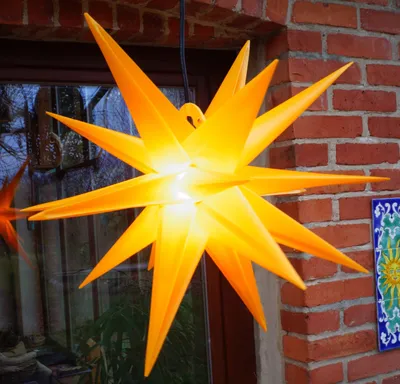 A bright yellow star-shaped lantern hangs in front of a brick wall and a window.