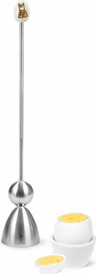 A stainless steel egg topper with a decorative top, next to a white egg cup holding a halved egg.
