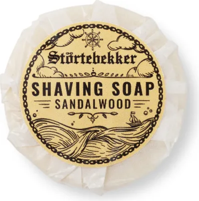 A round bar of sandalwood shaving soap, wrapped in white paper, with a decorative label featuring a nautical theme.