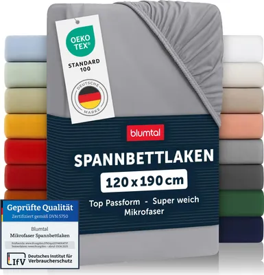 A folded grey fitted sheet is displayed prominently, with a stack of other colored fitted sheets visible on the left and right sides. Several labels and text overlays provide product information.